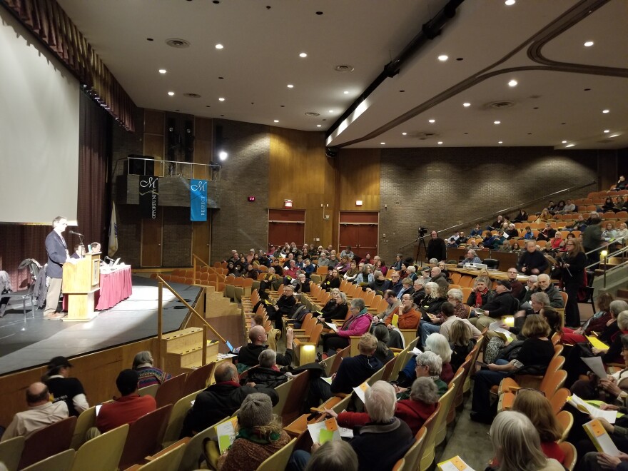 A auditorium filled with seated people facing a stage with people on it