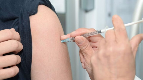 health worker sticks syringe into arm of a person with rolled up black sleeve