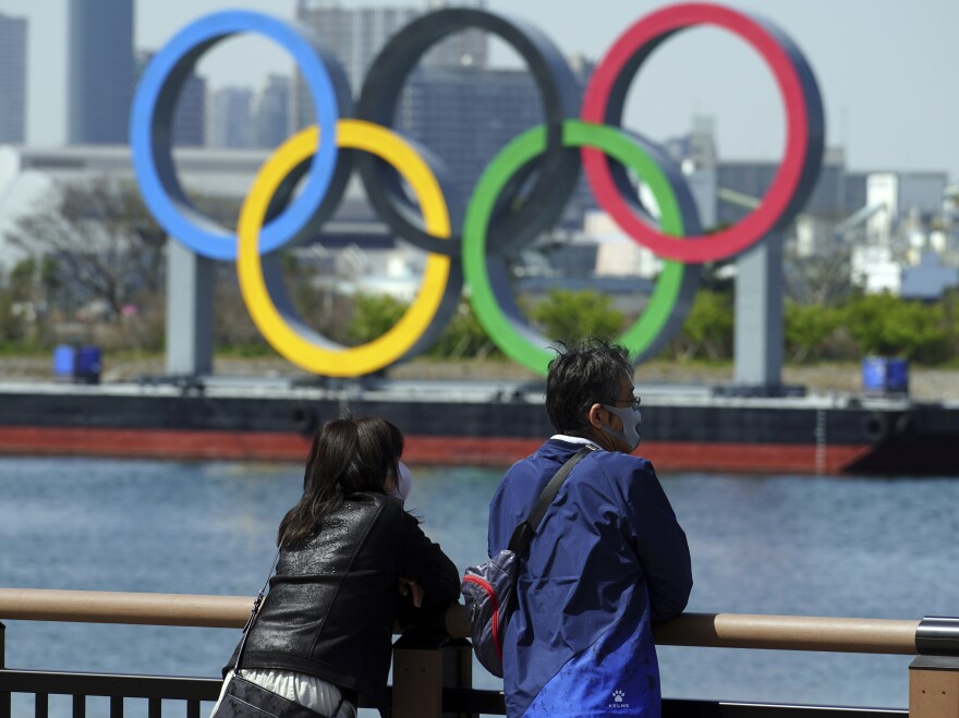 A man and a woman stand with a backdrop of the Olympic rings floating in the water in Tokyo on Thursday.