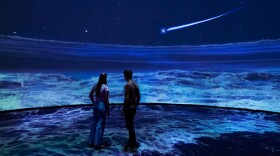 Man and woman stand inside museum 360 project with ocean covering them 