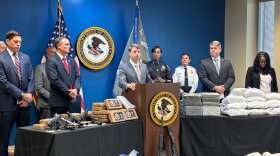Law enforcement officials standing at table with drugs and guns