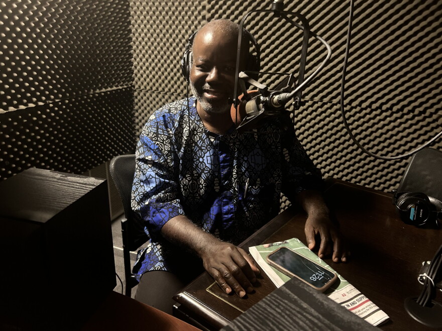 A man wearing headphones smiles while seated at a microphone.