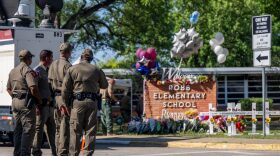 Law enforcement officers stand looking at a memorial following a mass shooting at Robb Elementary School in Uvalde, Texas.