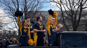 Michigan cheerleaders in maize and blue uniforms cheer with the crowd as the parade begins.