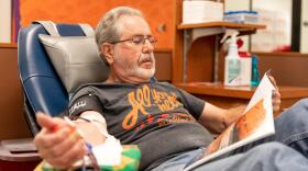 A man reads a magazine while donating blood.