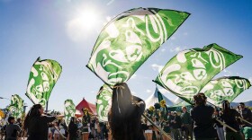 Color guard members, dressed in black, wave green flags with a white ram logo on them.