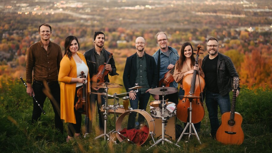 The OK Factor and Jaerv music ensembles standing together with their instruments on a scenic mountain with trees