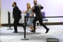 two men in black suits and a woman in a light blue dress running in a hallway. the woman is not wearing shoes