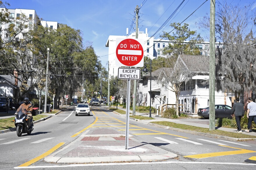 Pedestrians and a motorcyclist walk past one-way signage visible on Tuesday at the traffic circle at the intersection of Southwest Second Avenue and Southwest 12th Street in Gainesville.