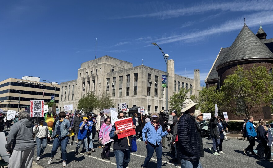 A photo of people carrying signs walking in downtown Greensboro for the city's third No Kings protest.