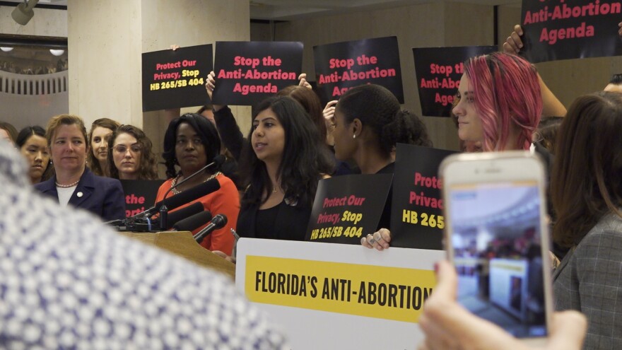 Eskamani stands at a podium with young adults from Planned Parenthood crowded around her. These adults hold signs that read, "Stop the Anti-Abortion Agenda," and "Protect Our Privacy, Stop HB 265/SB 404."