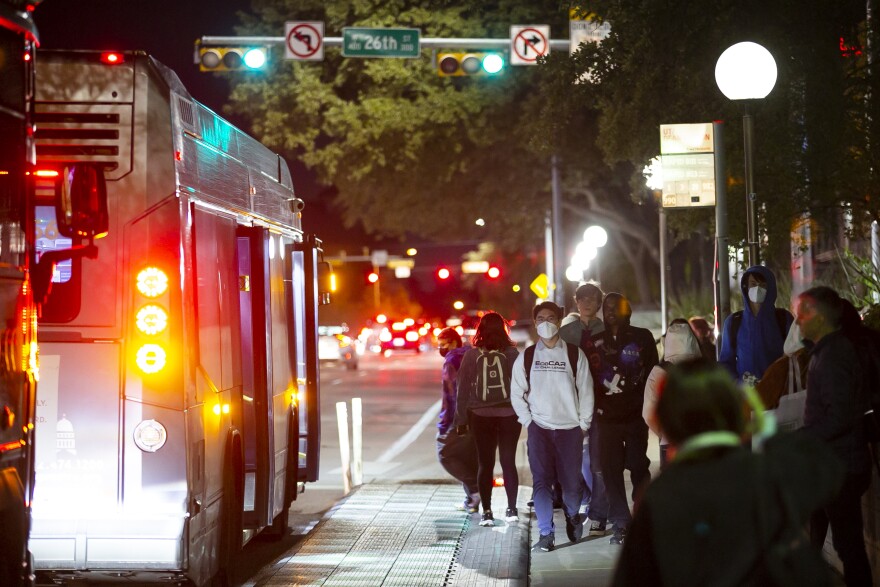 A Capitol Metro bus approaches a group of people as they wait at a CapMetro bus station on Guadalupe Street at the University of Texas on Nov. 15, 2022.