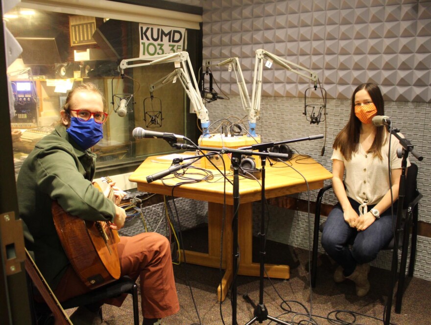 Man with a guitar and seated woman, both wearing cloth face masks