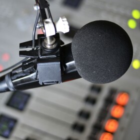 A microphone in focus over an out-of-focus soundboard.