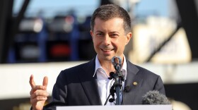 A man at a podium, gesturing with his hand.