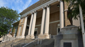 The front of a brown brick and stone building with columns, stairs and statues of soldiers.