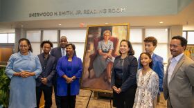 The Allen family poses together in front of the portrait of Sylvia Allen.