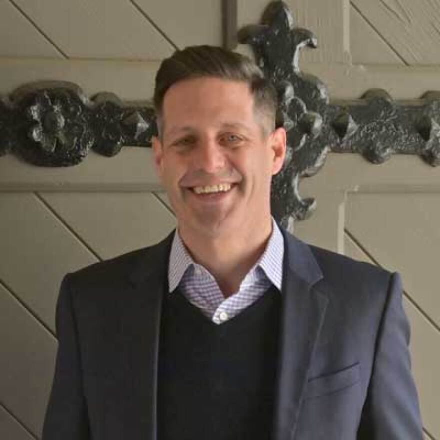 a man wearing a suit and sweatervest, smiling