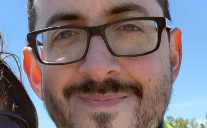 A smiling man with short brown hair with a brown mustache and beard, wearing glasses and a lime colored shirt