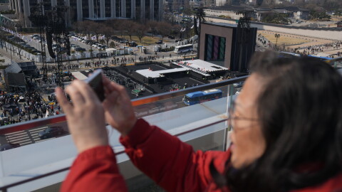 A woman films with her smartphone near a stage for a concert by K-pop group BTS at Gwanghwamun Square in Seoul, South Korea, Friday, March 20, 2026.