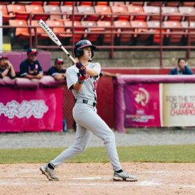 London Studer wears a gray baseball uniform and looks to the sky as she prepares to swing a bat.