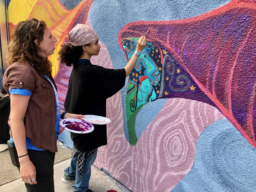 Amy Ruza, youth and visitor engagement educator for The Rockwell Museum guides current C-PP High School Learning Center student, Nagi Estrada as he paints a portion of the 2025 Alley Art Project mural, "Colorscape."