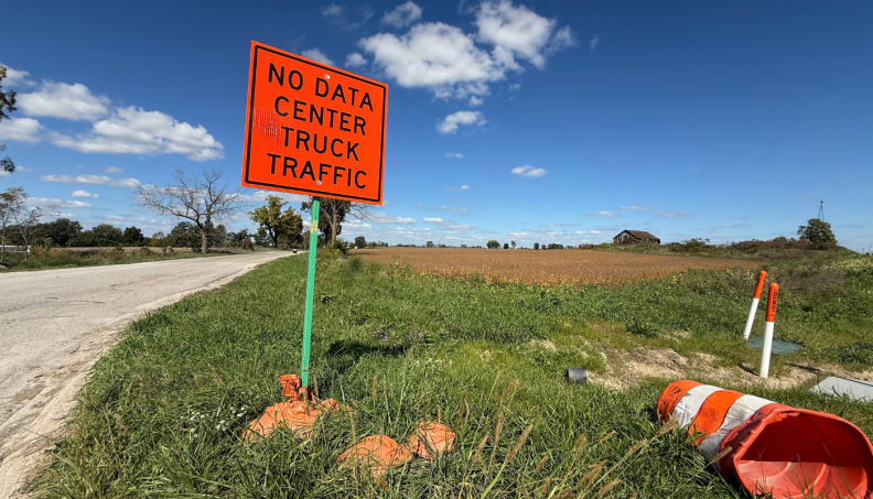 an orange traffic sign says "no data center traffic" stands in a field of grass with a blue sky behind it
