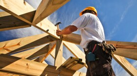 A man hammers wooden beams together on a construction site. 