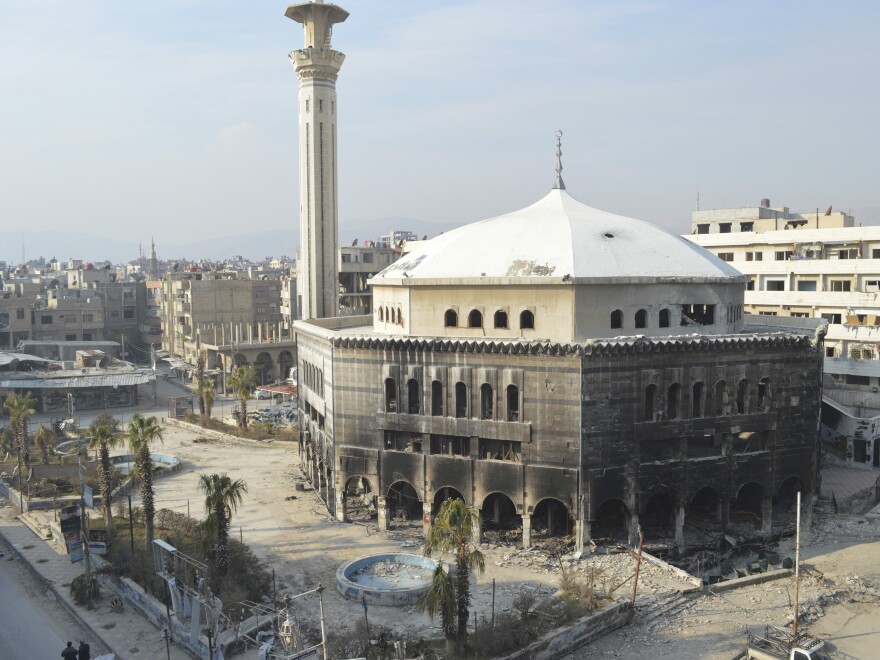 Residents walk near a mosque damaged in recent violence in Douma, near the Syrian capital, Damascus. Activists say it was shelled by forces loyal to Syria's President Bashar Assad.