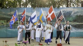 People on stage dressed in 1800s Scandinavian clothing, holding flags from each Scandinavian country. 