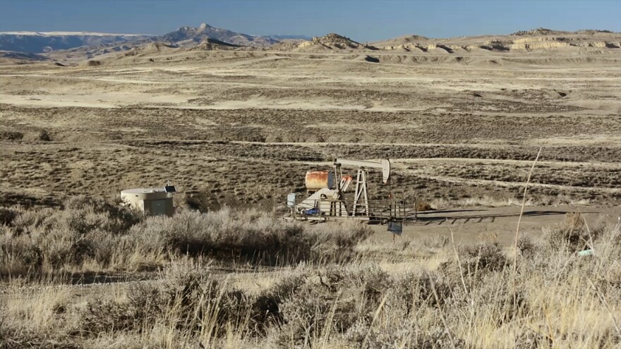 An oil rig in a brown field with mountains in the background in Wyoming