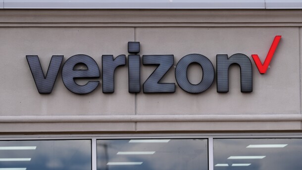 A close up shot of a black text Verizon sign, with a red check mark on the right side next to the text. The tops of windows can be seen at the bottom of the photo, which are mostly cropped out. 