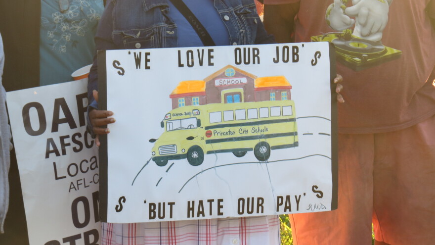 Close-up of a Princeton bus driver holding a sign that reads "We love our job, but hate our pay."