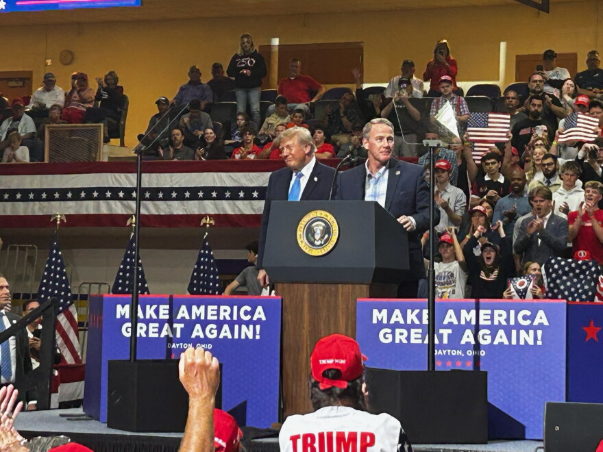 U.S. Sen Jon Husted and President Donald Trump stand on stage together at a rally in Vandalia, Ohio, with a crowd of supporters behind them