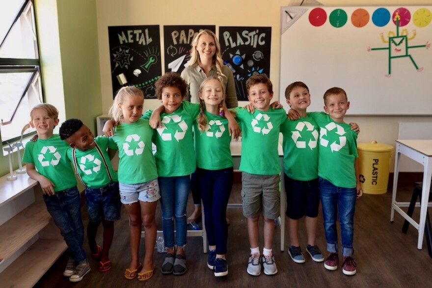A teacher stands behind a row of school children who are dressed in green T-shirts.