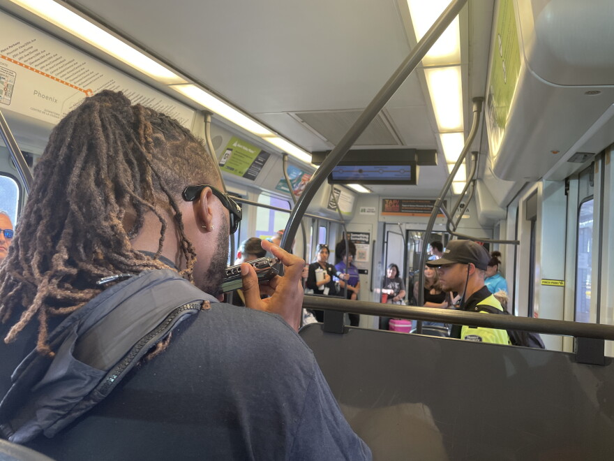 View from behind the shoulder of a man playing harmonica on a light rail train