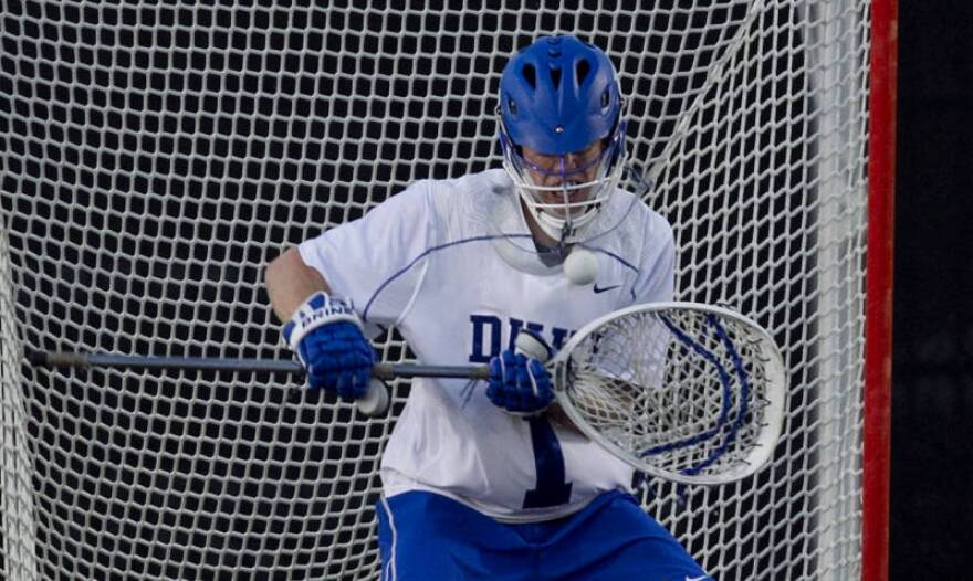 A Duke Blue Devil guarding the net in a lacrosse game against Virginia.