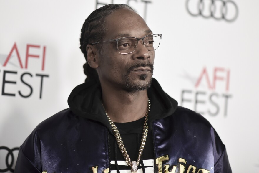 Snoop Dogg wears gold-rimmed glasses a black hoodie and a gold chain