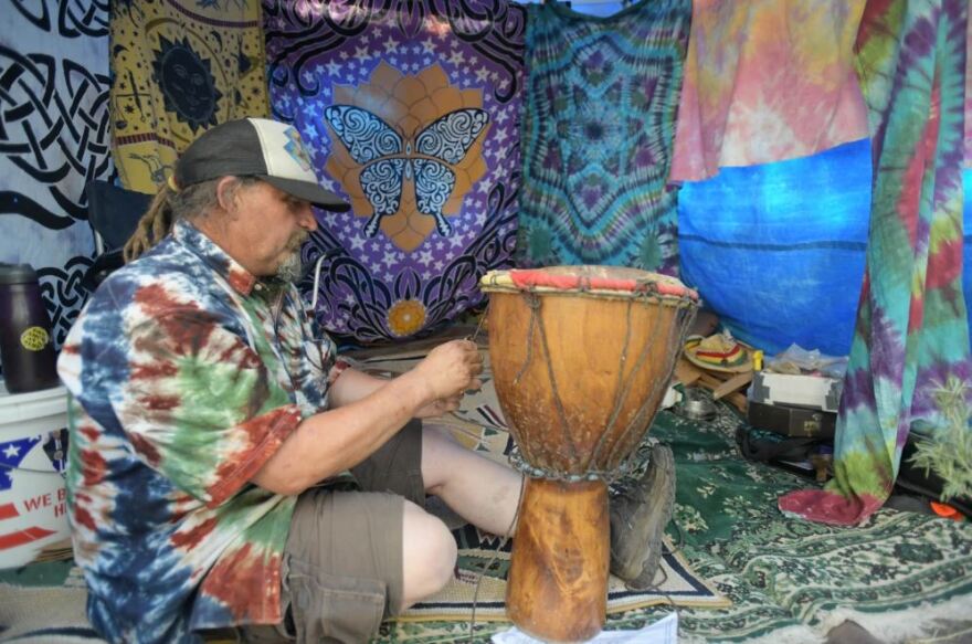 Rainbow Family member Kevin Lovinghawk, of Idaho, works on an African djembe drum July 3, 2022, in the Adams Park area of Colorado’s Routt National Forest. Lovinghawk attended his first Rainbow Family annual gathering in 1992.