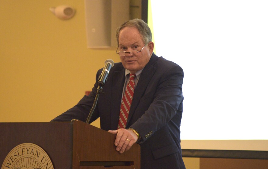 A man in a blue suit stands at a podium delivering a speech