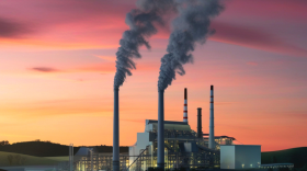 A power plant at sunset emitting smoke.