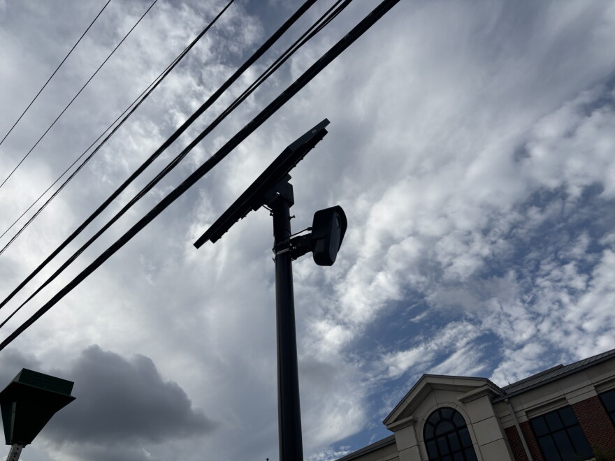 A Flock camera against a cloudy sky, with power lines and a brick building in the background.
