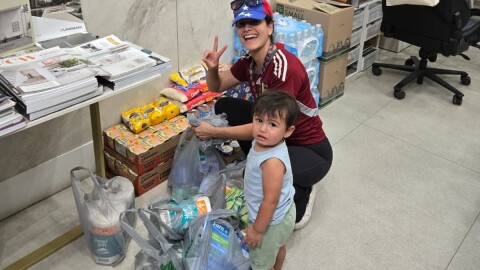 A woman and a young boy are next to grey plastic bags filled with supplies like paper towels.