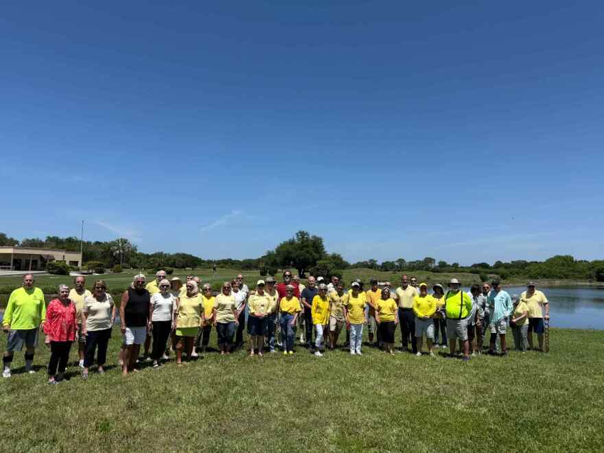 A group of men and women stand outside at a golf course with a lake in the background 