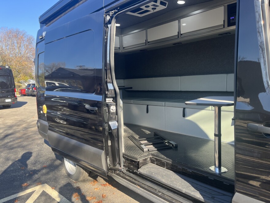 A look inside one of the large, black vans used by the police department and the social services unit. The sliding door reveals lots of seating, small middle tables and television screens and storage units around the inside of the vehicle.