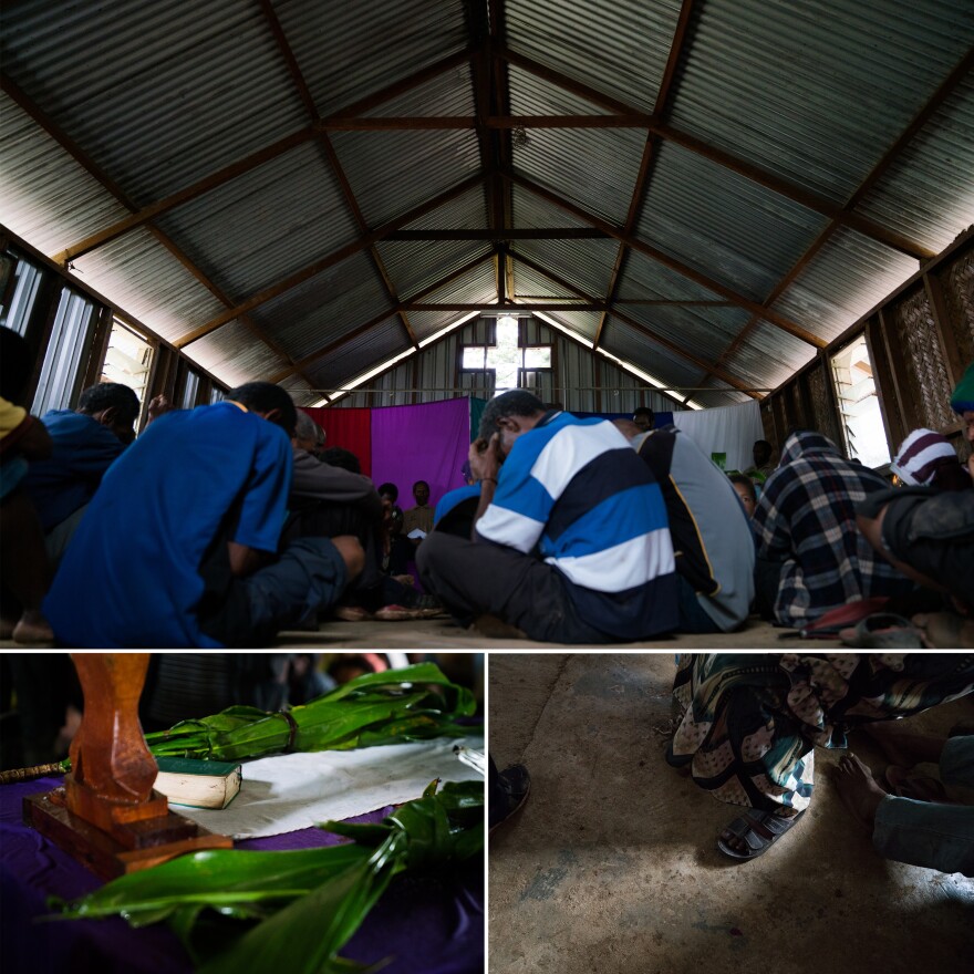 People bow their heads during a prayer at the reconciliation meeting in Henganofi. Leaves of the tanket plant and a Bible are set on a table in the center of the room.