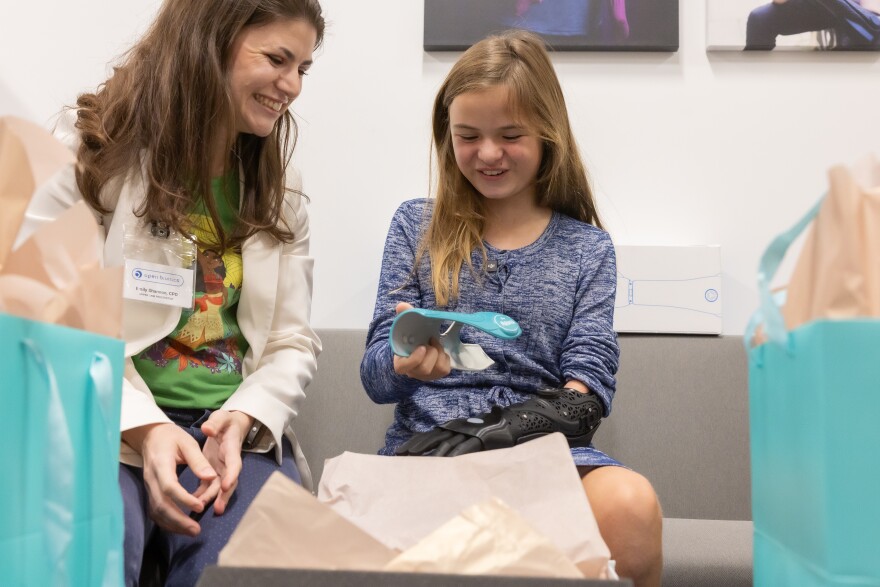Eloise Bayliss, 12, holds an attachment for her bionic arm, sitting next to Emily Shannon, a prosthetist with Open Bionics, who worked on Eloise's arm.