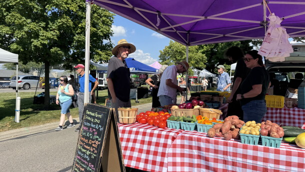 People standing by a booth with a variety of produce products and two vendors.