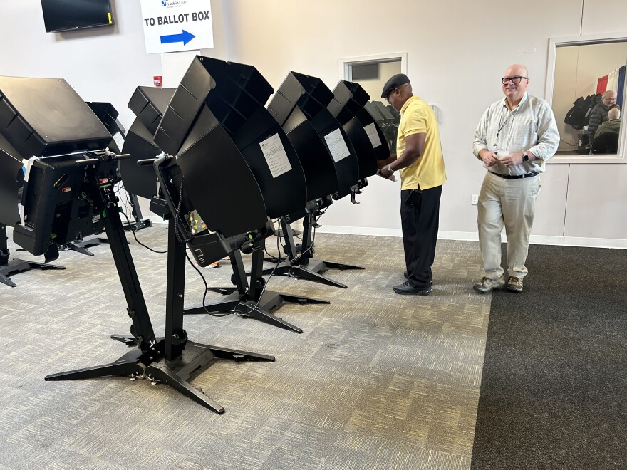 A man votes at a row of voting booths while a pollworker stands nearby.