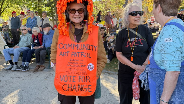 A woman wears a sign as other protesters gather behind her.
